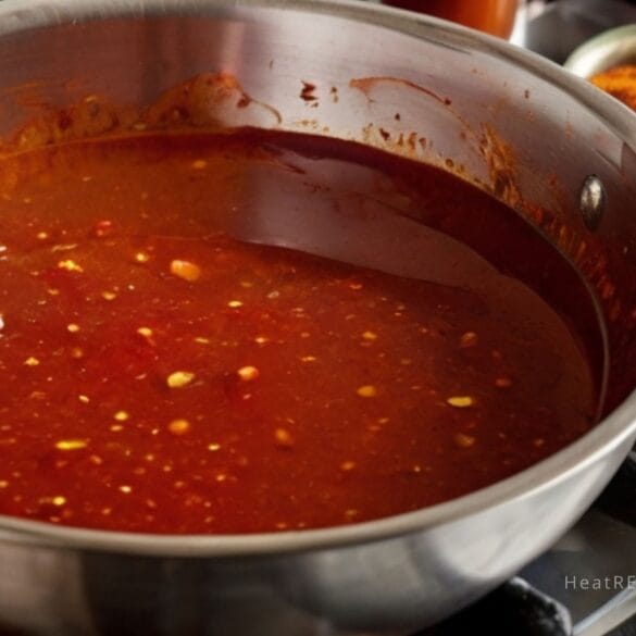 The sauce is rich red and is being prepared with a focus on intense heat and flavor.