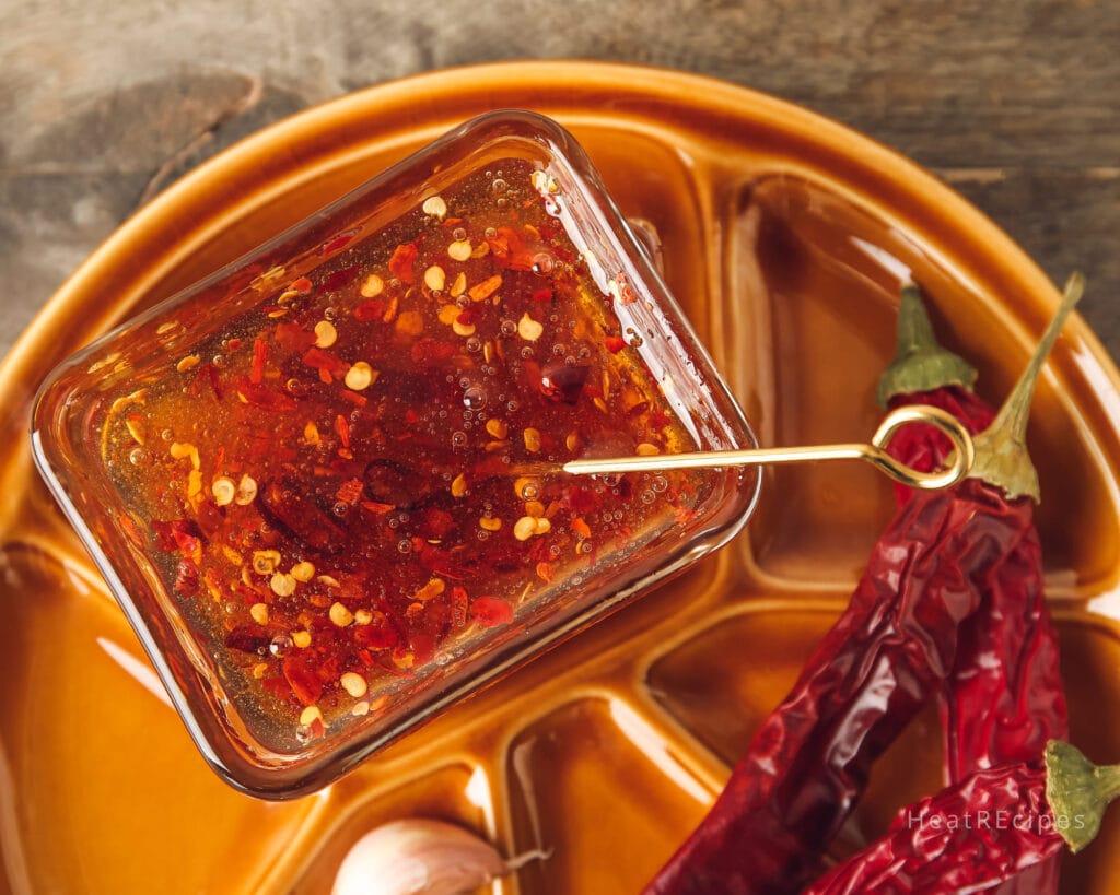 A jar of homemade hot honey sauce, featuring sweet honey and sliced chili peppers, perfect for drizzling over fried chicken or pizza for a sweet and spicy flavor